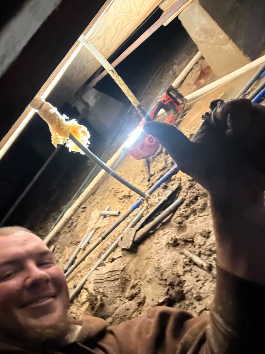 Plumbing tech taking a smiling selfie in a crawlspace