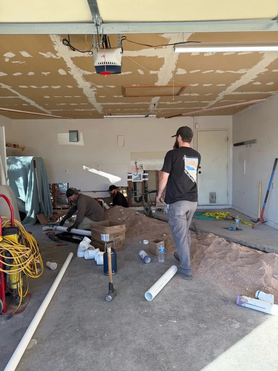 Plumbing crew working on a slab sewer repair inside a garage