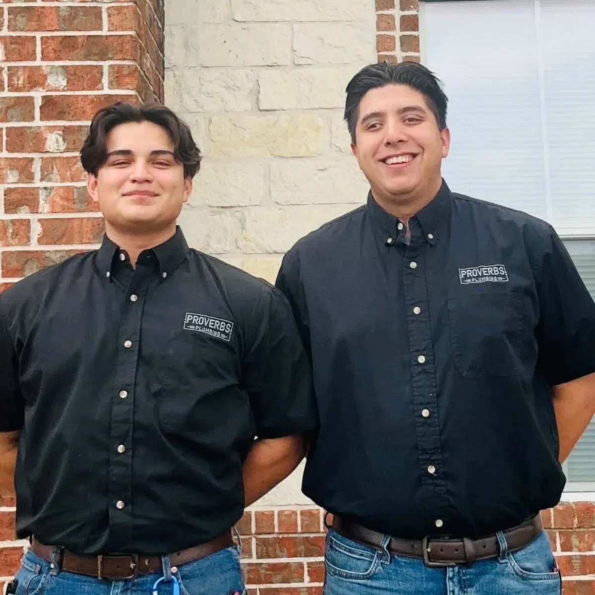 Two smiling plumbing techs in black company shirts