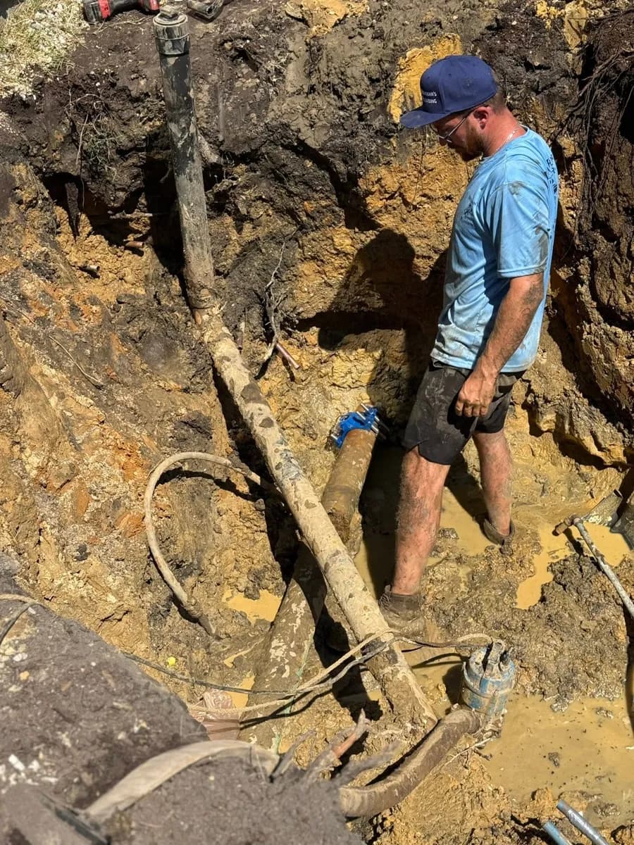 Plumbing tech standing in a dug-out trench repairing a water line